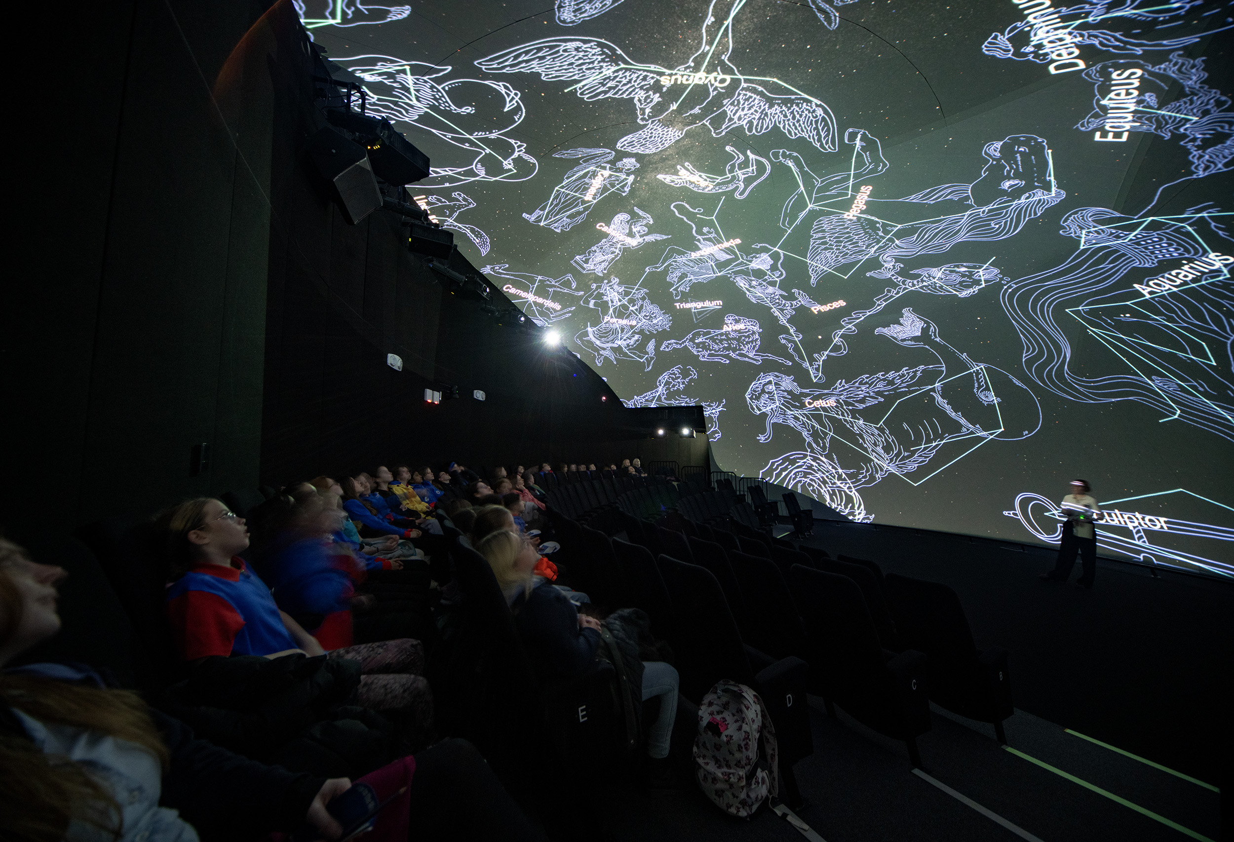 A photo of a group of girl guides sat in the curved Space Dome, observing constellations.