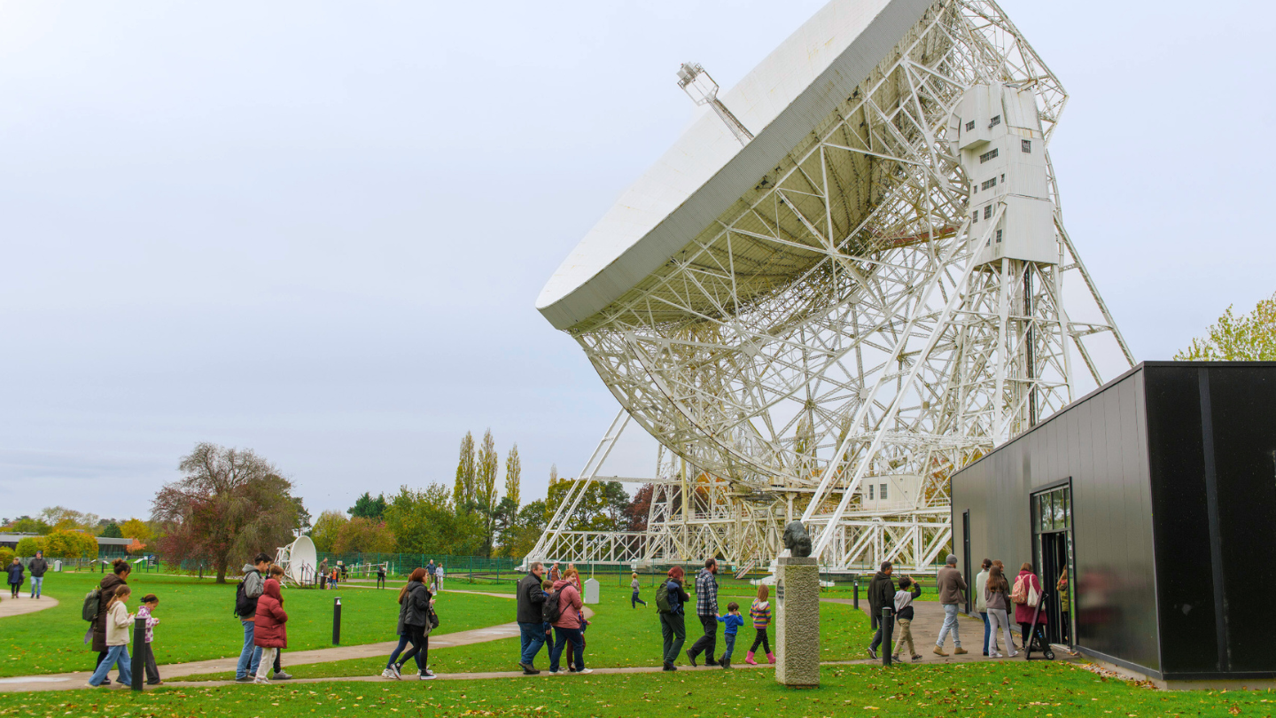 Visitors walk into a black building with the Lovell Telescope in the background.
