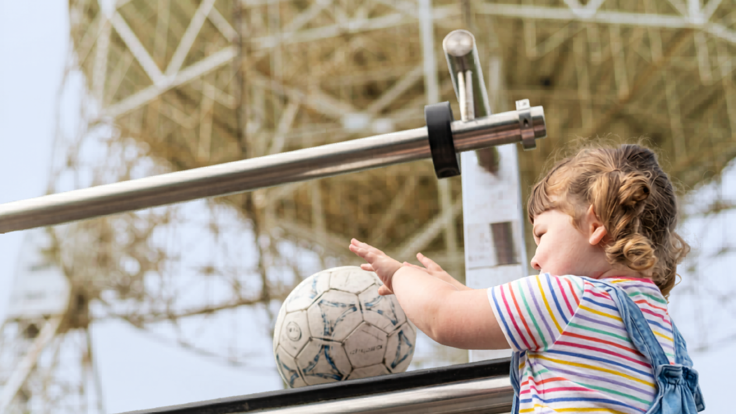 A child with pigtails and dungarees pushes a football experiment in front of the Lovell telescope.