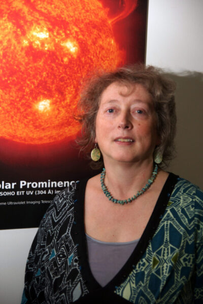 A photo of Prof Philippa Browning, a woman with brunette hair in front of a picture of the sun.