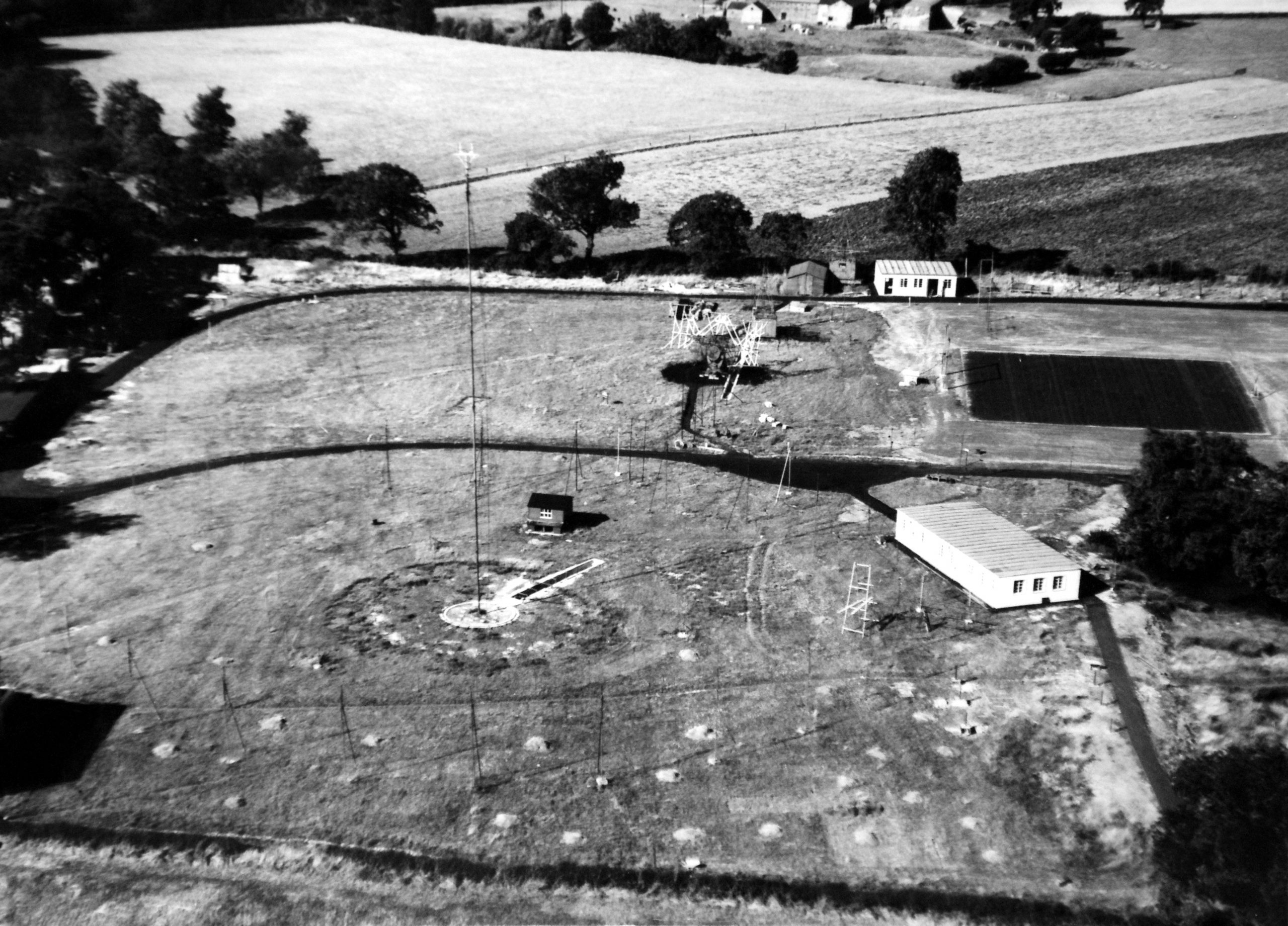 Black and white aerial view of the site, showing the Transit telescope, the Searchlight aerial, the Park Royal hut and Moon hut.