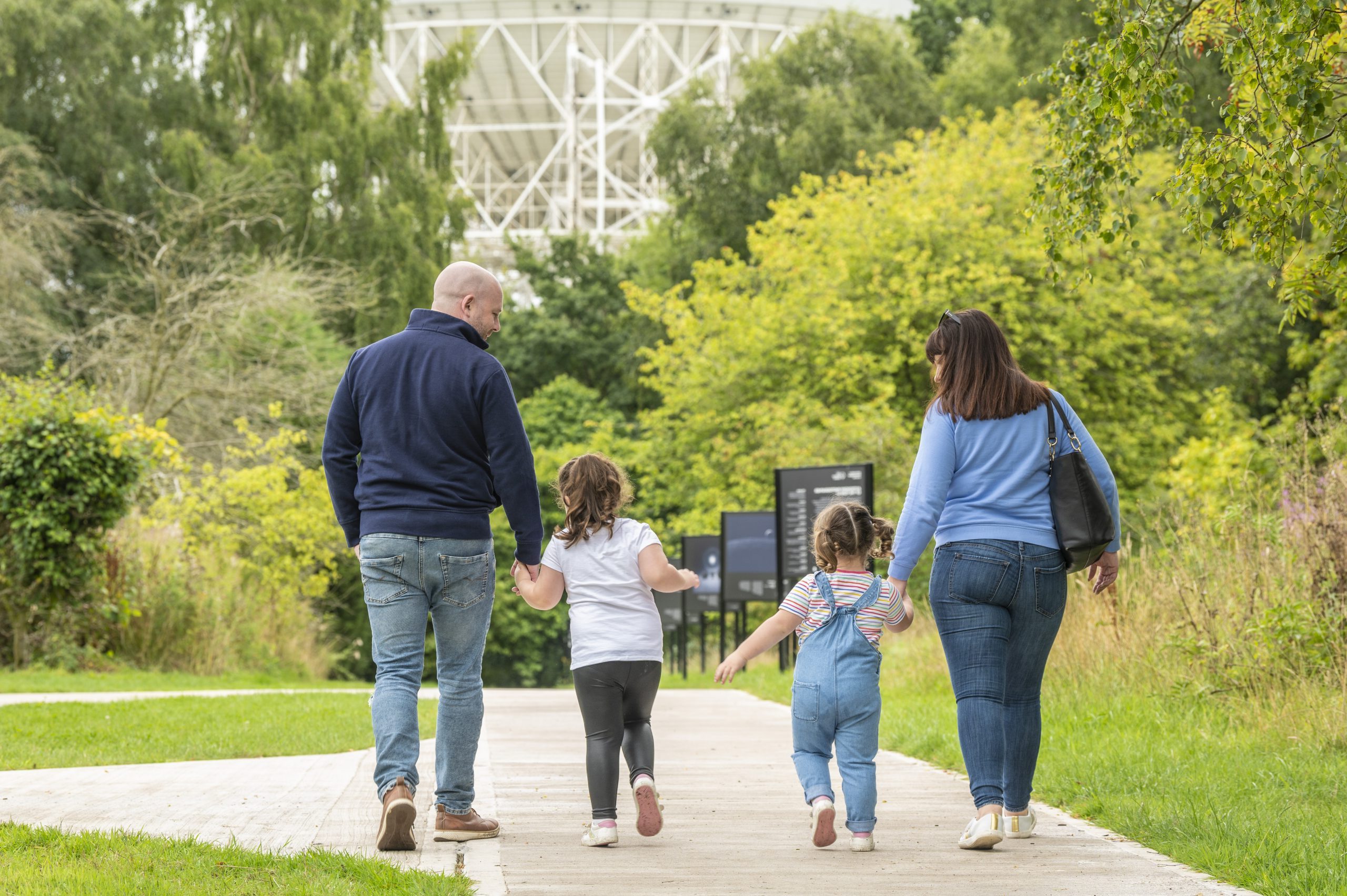 A photo of a family of four holding hands and walking towards the Lovell Telescope.