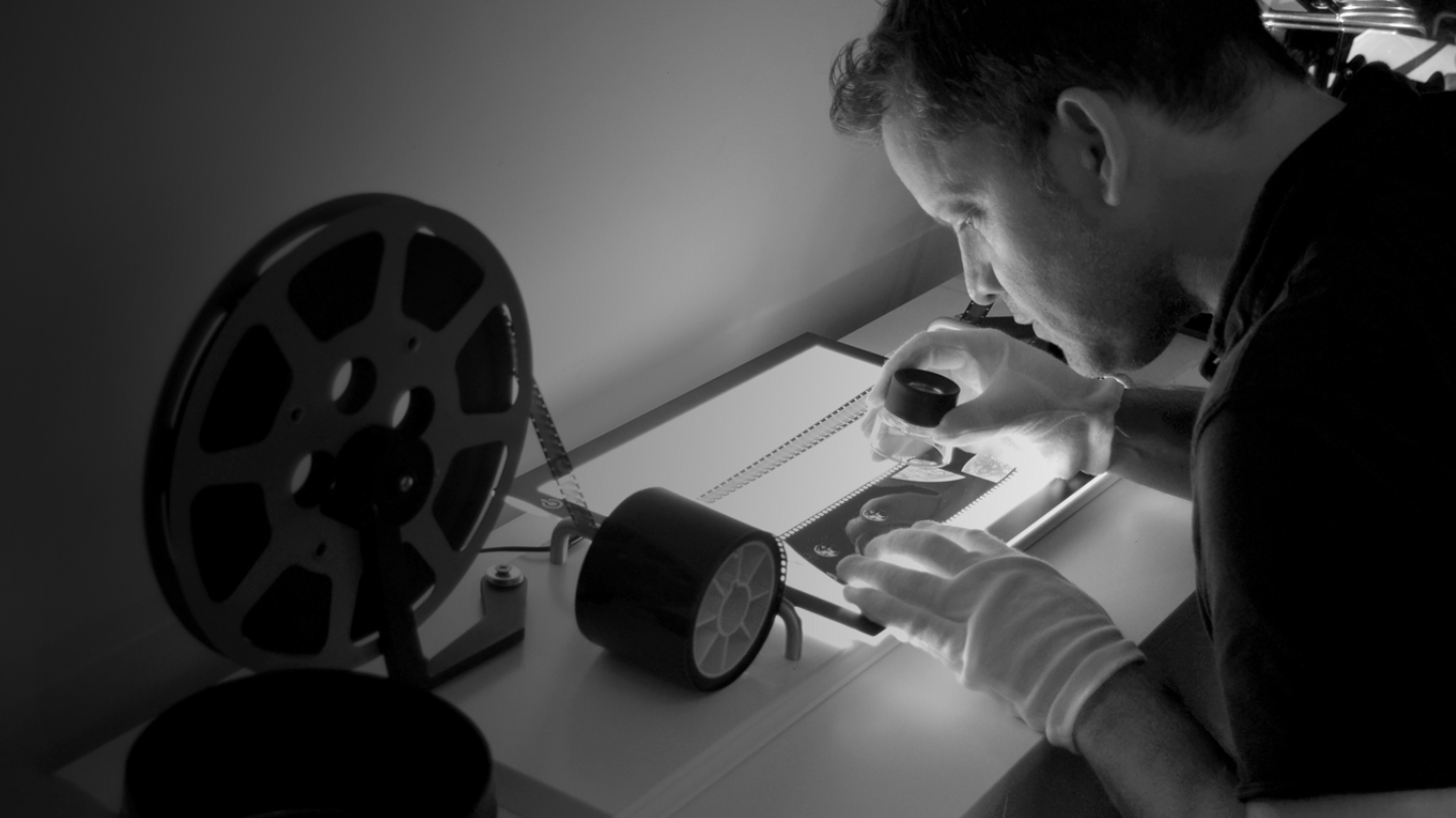 A black and white photo of Andy Saunders performing digital restoration work.