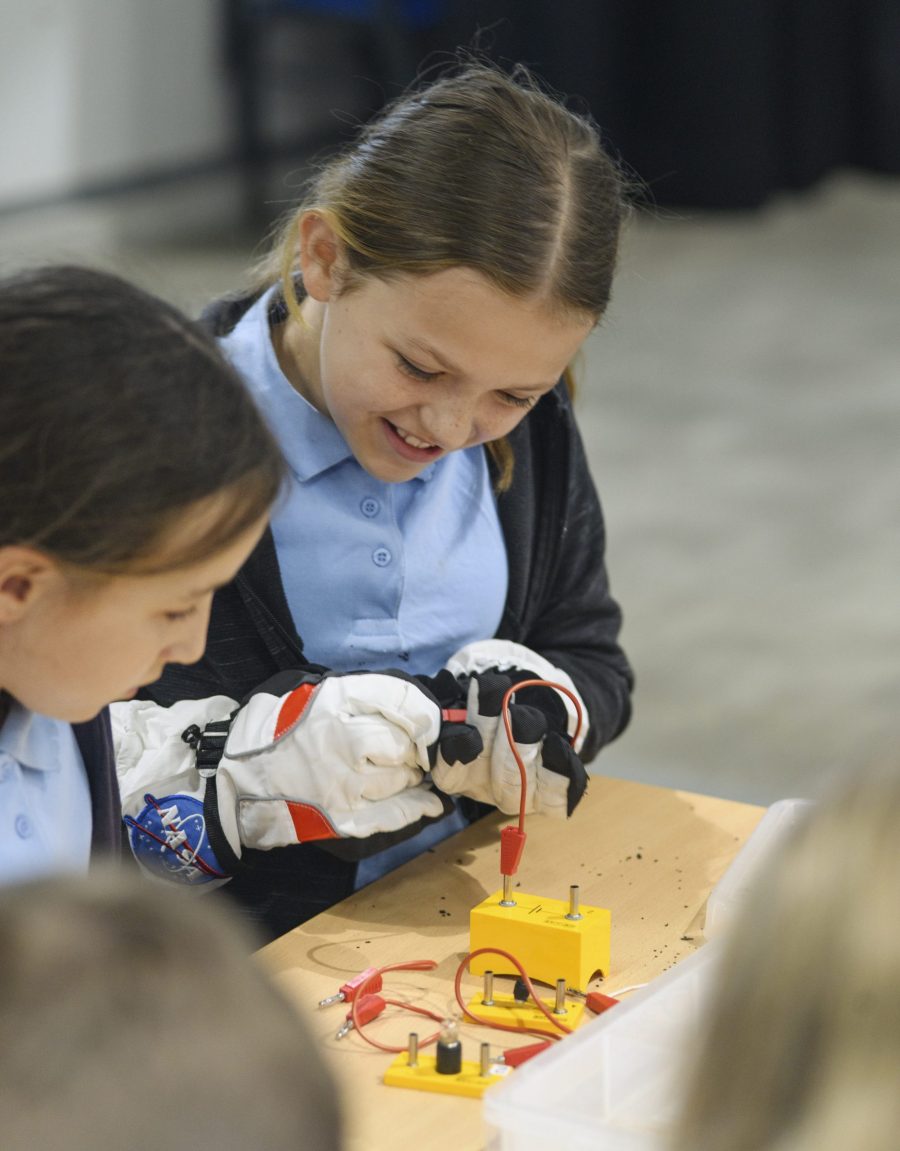 Primary school children wiring a circuit in astronaut gloves.
