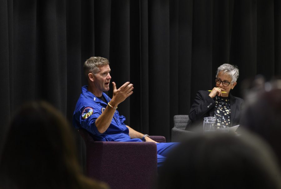 John McFall, a man in a blue ESA spacesuit, sat at a table in front of a crowd with JBCE Director, Teresa Anderson.