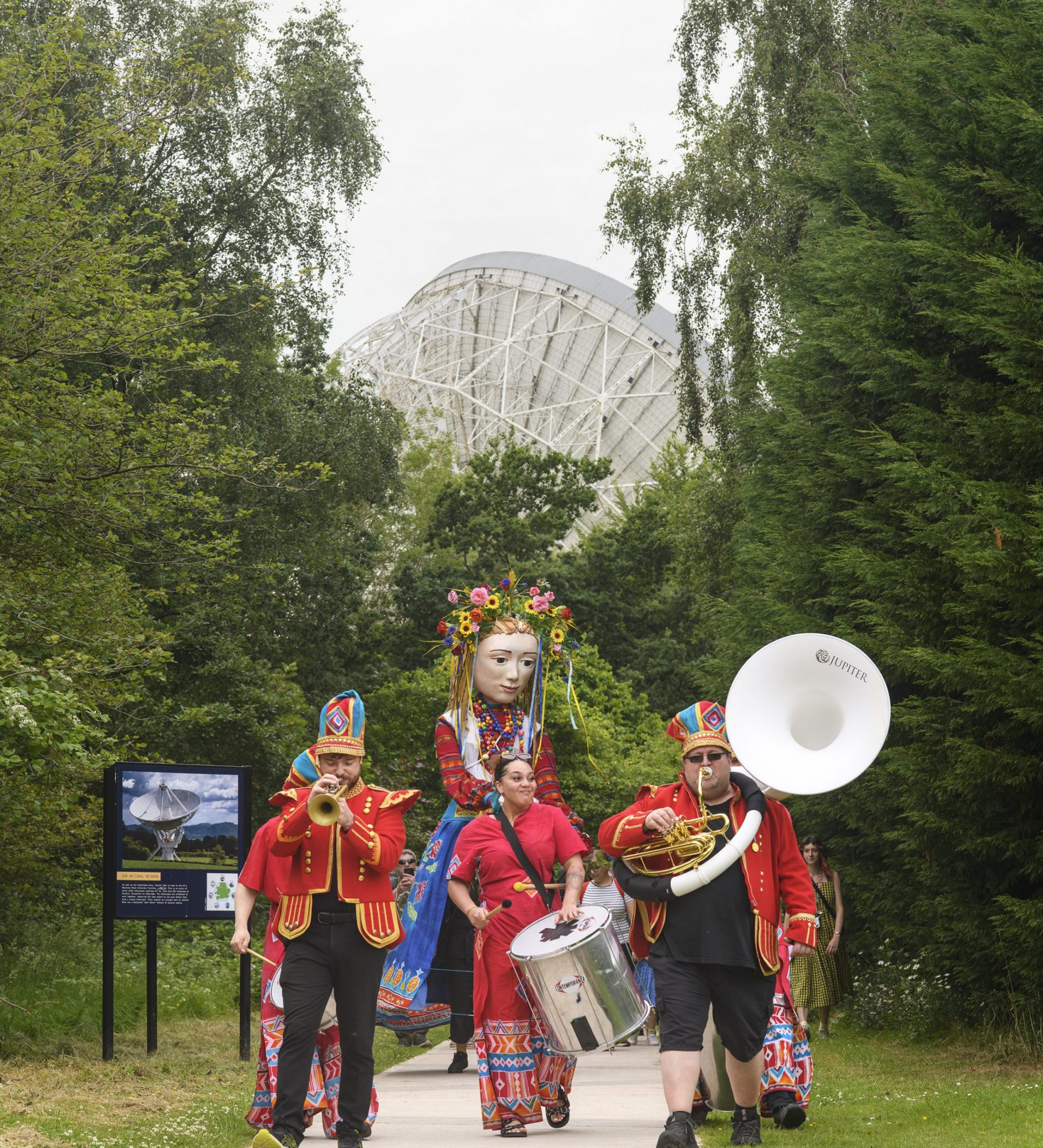 Global Grooves carnival procession - including a brass band a giant, colourful puppet, in front of the Lovell telescope.