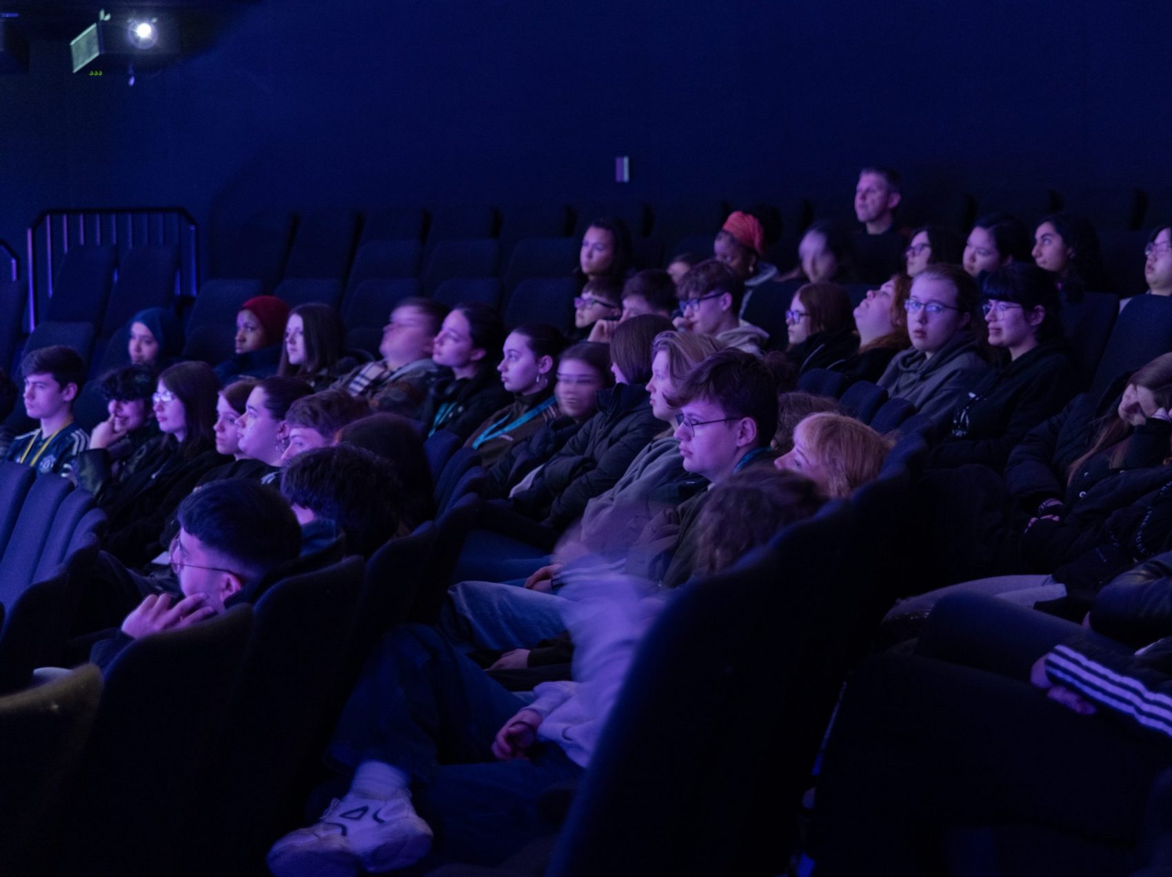 A photo of a group of people in the Space Dome, watching a purple-tinted screen.