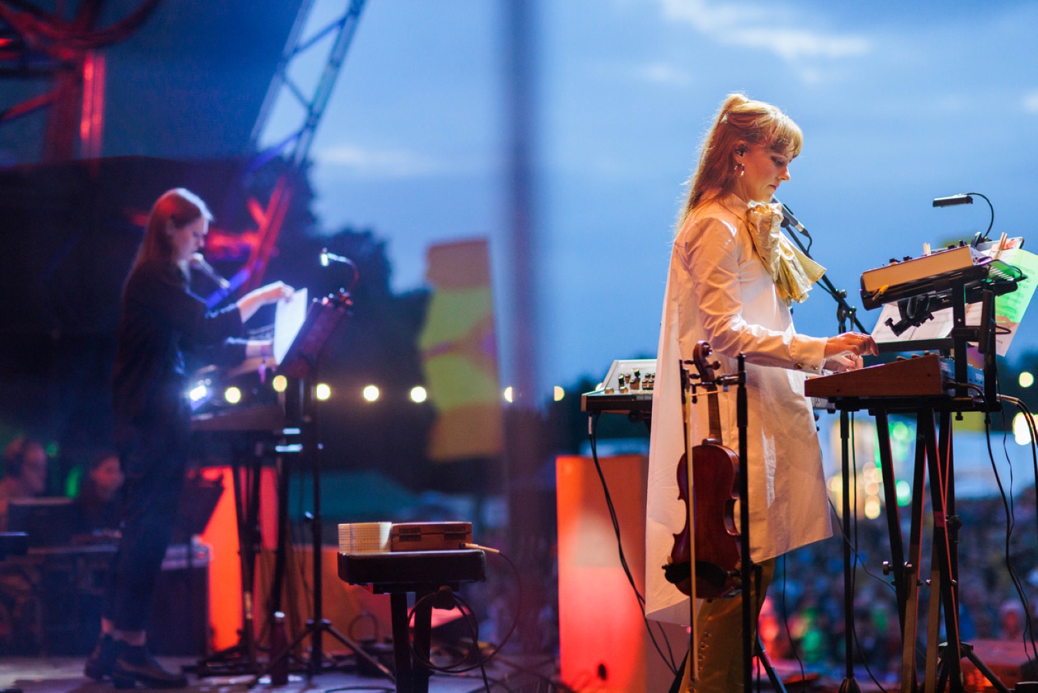 Hannah Peel, a women in a white dress with red hair, performs on stage at an evening concert.