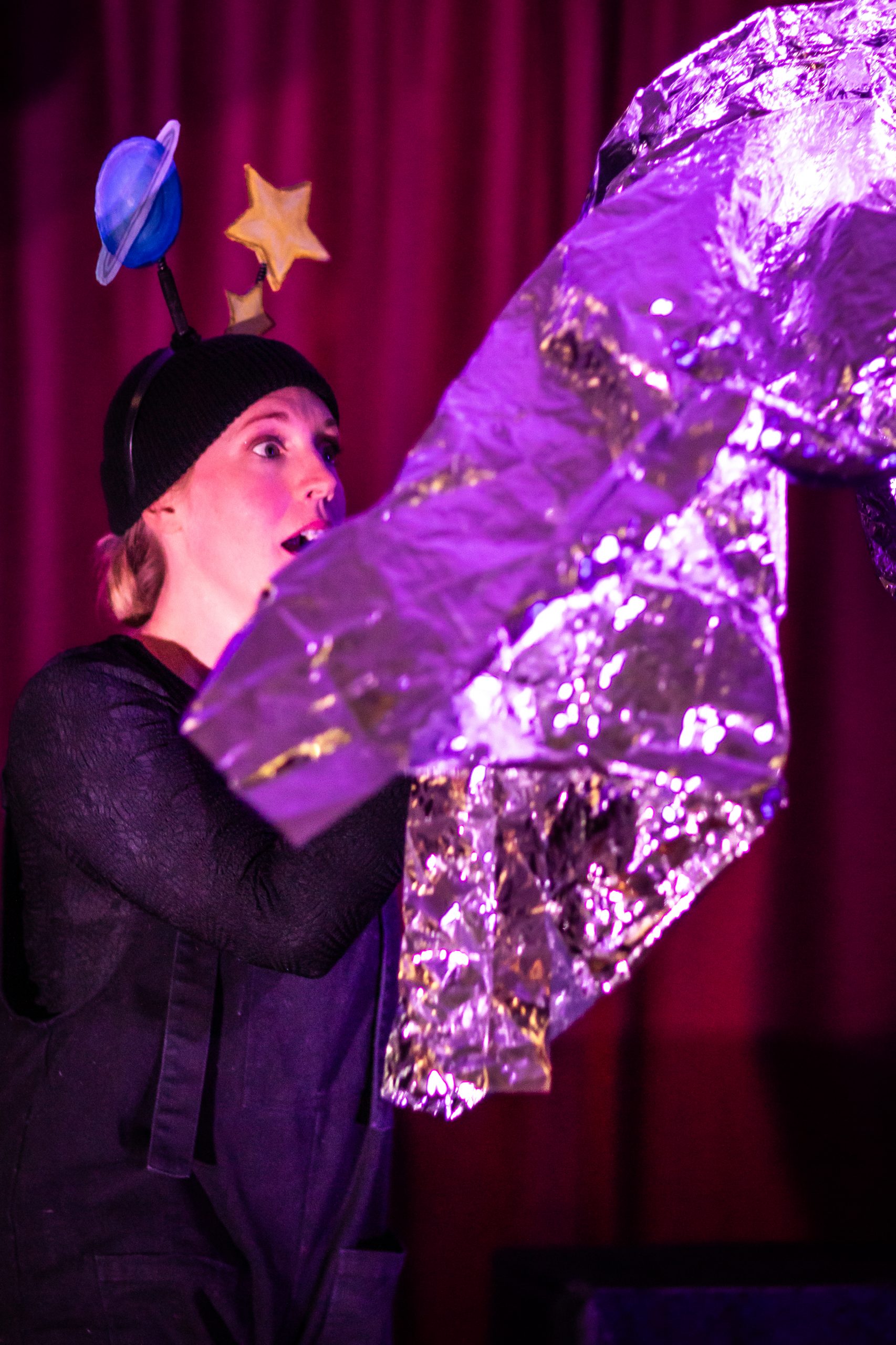 A woman performs with a tinfoil rocket on stage. Credit: Goofus Theatre. All in a Mouse's Night.