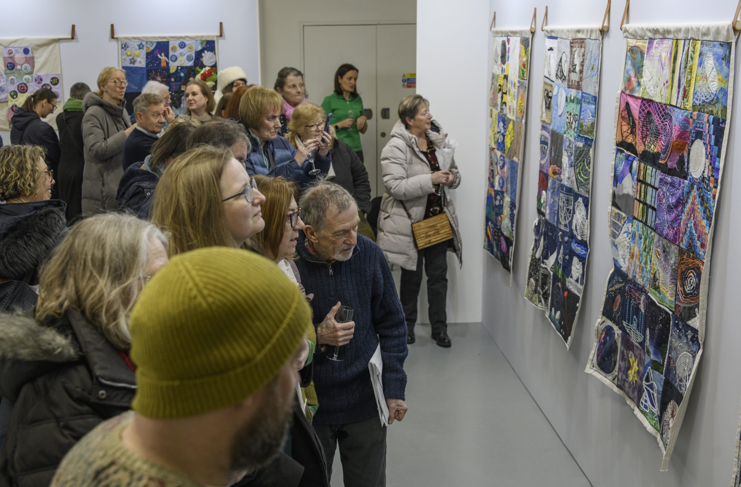 A group of visitors enjoy the colourful collection of hanging textile quilts, showing various squares depicting Jodrell Bank and space.