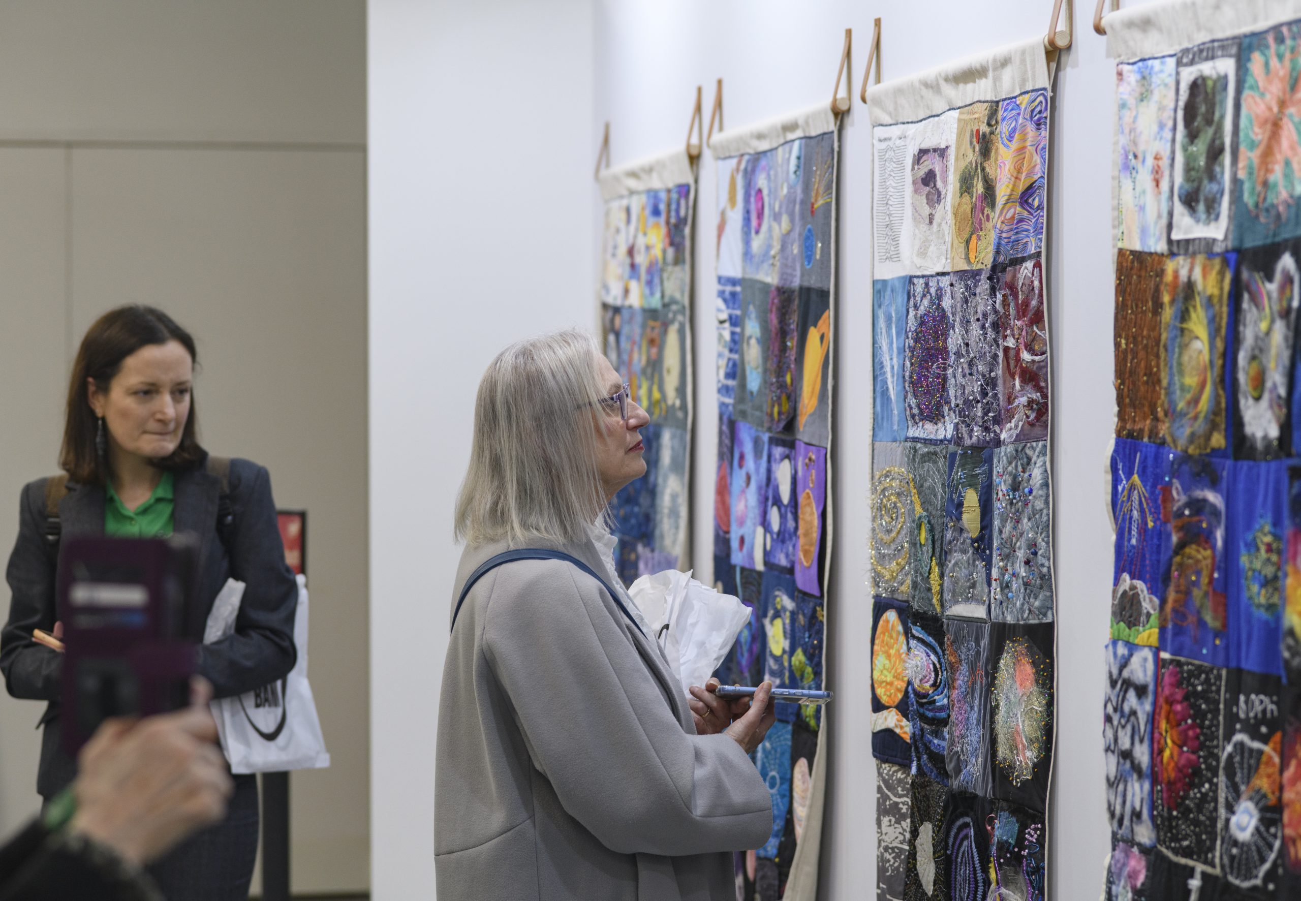 A group of visitors enjoy the colourful collection of hanging textile quilts, showing various squares depicting Jodrell Bank and space.