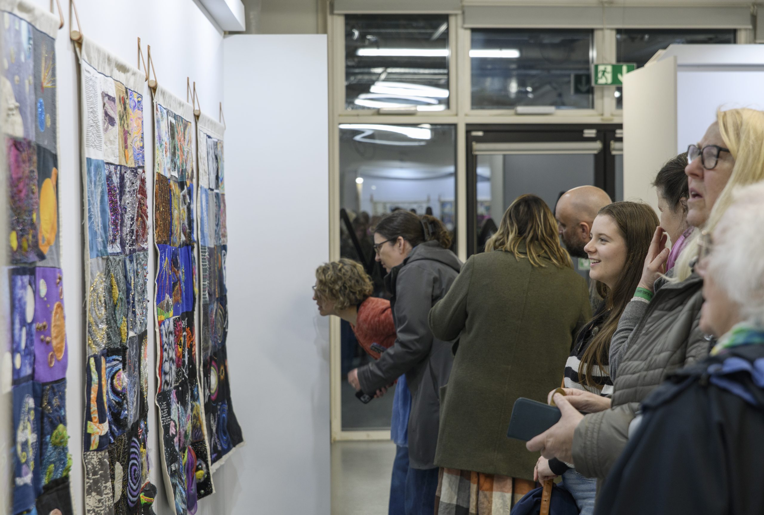 A group of visitors enjoy the colourful collection of hanging textile quilts, showing various squares depicting Jodrell Bank and space.