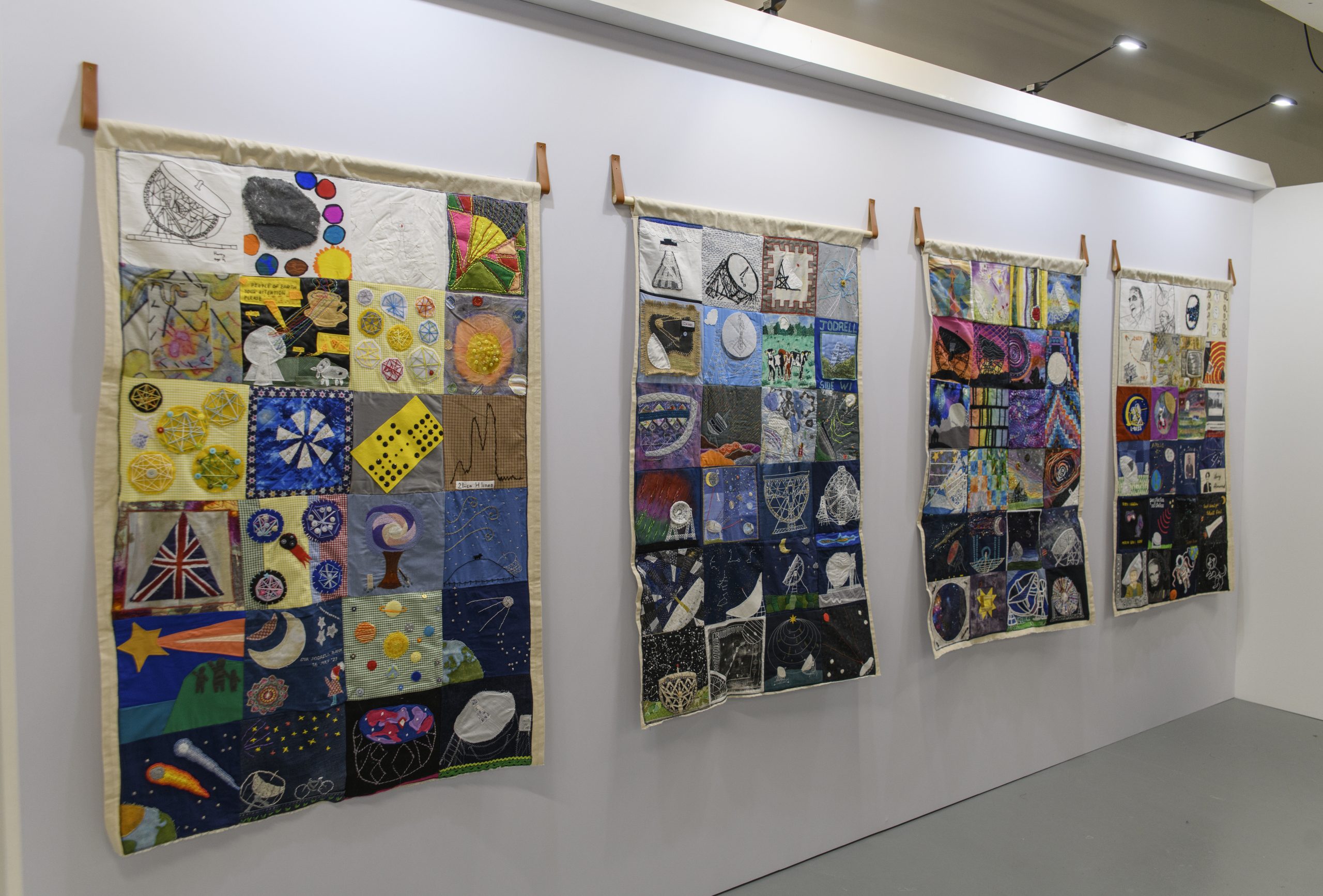 A wide shot of four of the quilts hanging side-by-side within the exhibition.