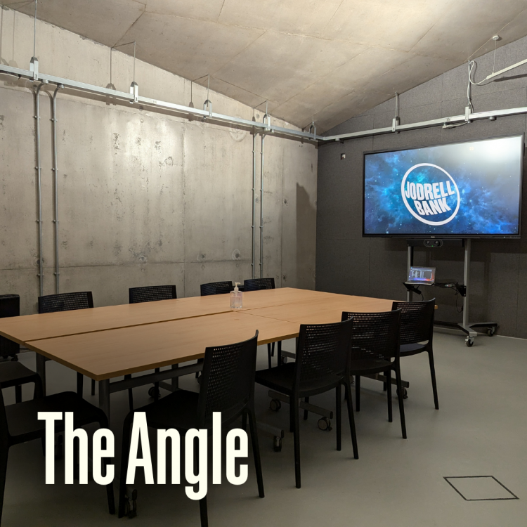The Angle meeting room with a large wooden conference table, black chairs and concrete walls. A screen displaying the 