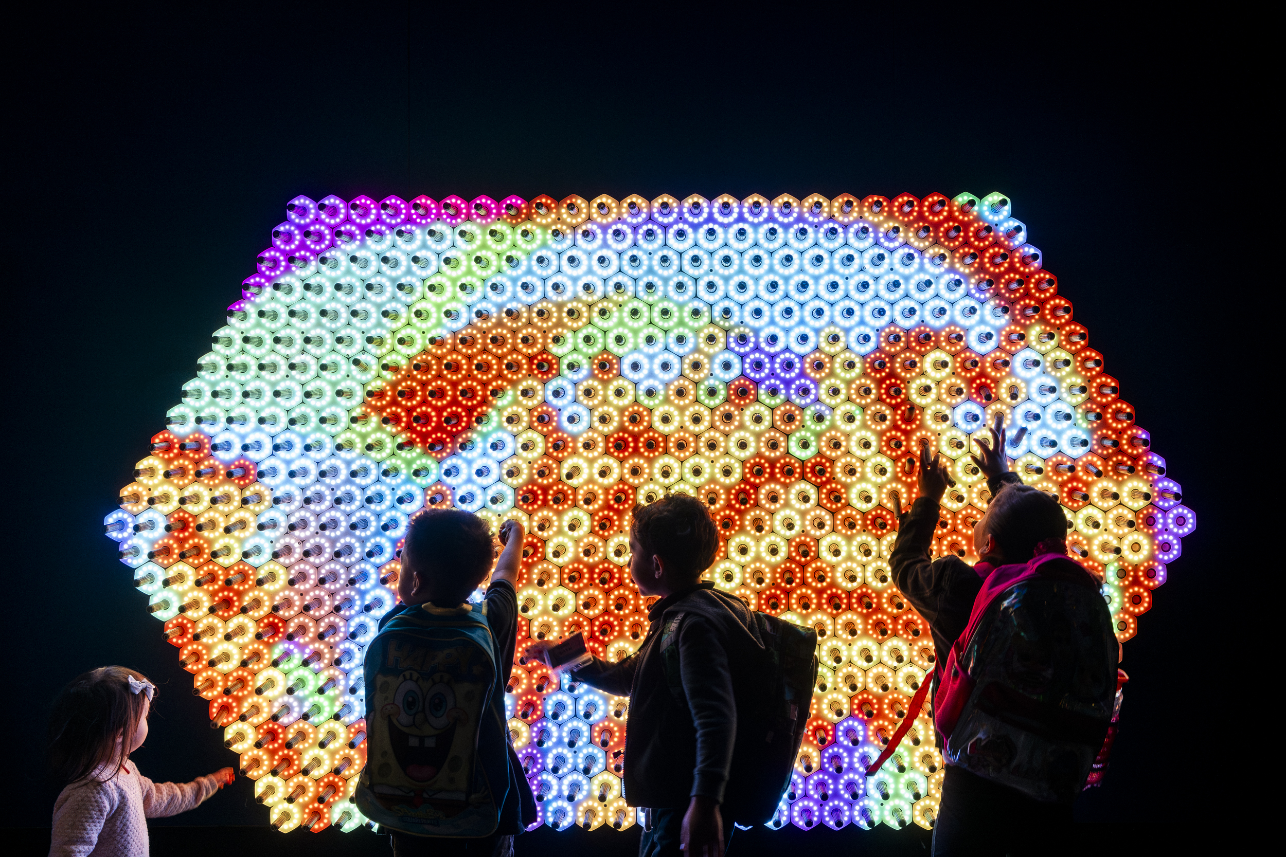 Four children interact with an LED light exhibition, filled with colourful shapes, as part of Quantum Jungle.