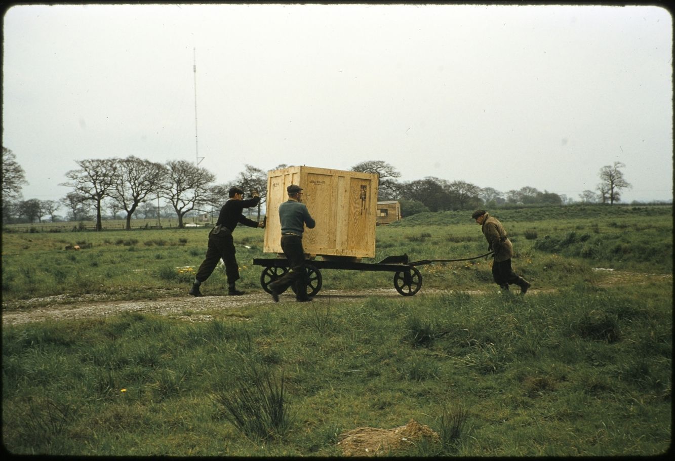 3 gentlemen pushing a card with a large wooden crate on top