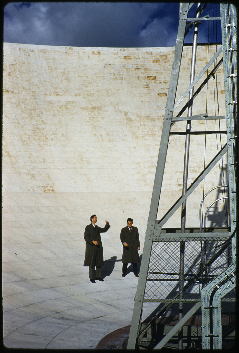 Two men stood inside the dish of the Lovell Telescope, 1 pointing to the structure