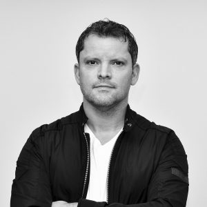 A black and white photo of Andy Saunders, a man with short hair, a black jacket, and white shirt.