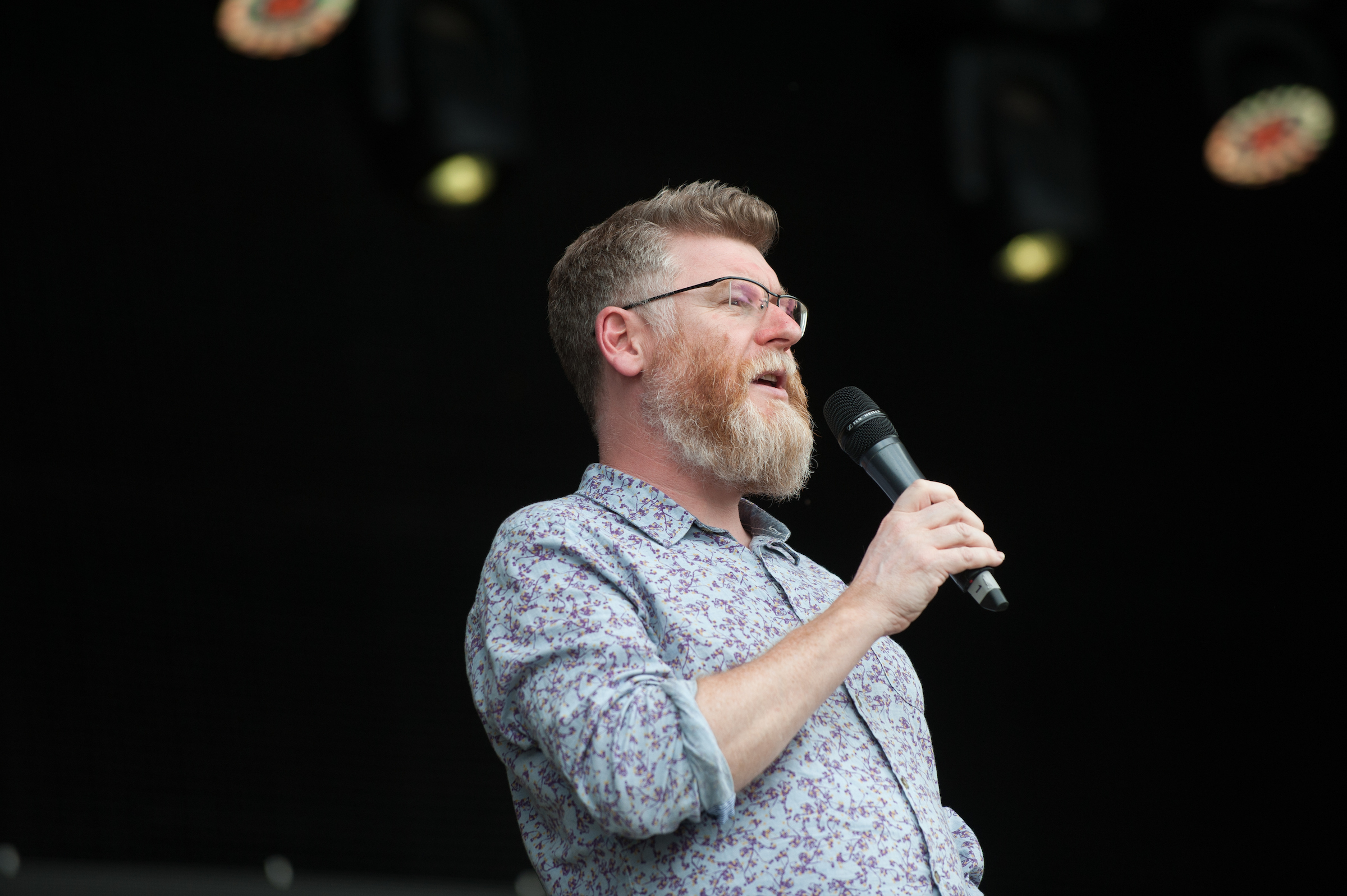 A photo of Professor Tim O'Brien, a man in a patterned shirt with a beard and glasses, holding a microphone.